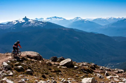 A mountain biker rides through the scenic landscapes of British Columbia, Canada, surrounded by majestic mountains and clear blue skies, showcasing the beauty of nature and sport.