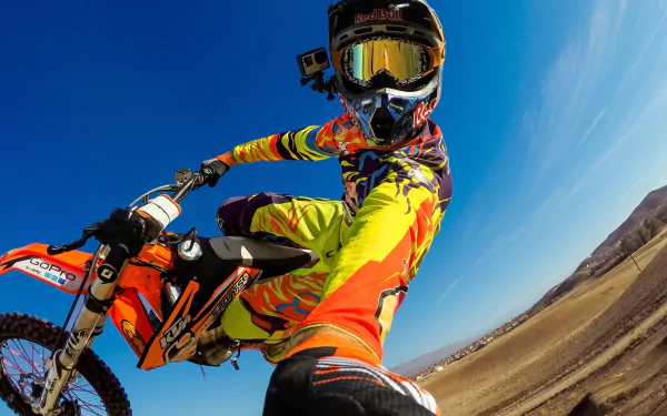 A dynamic motocross rider performs a jump against a clear blue sky, showcasing vibrant gear and a thrilling sense of speed, capturing the essence of sports in an HD desktop wallpaper.