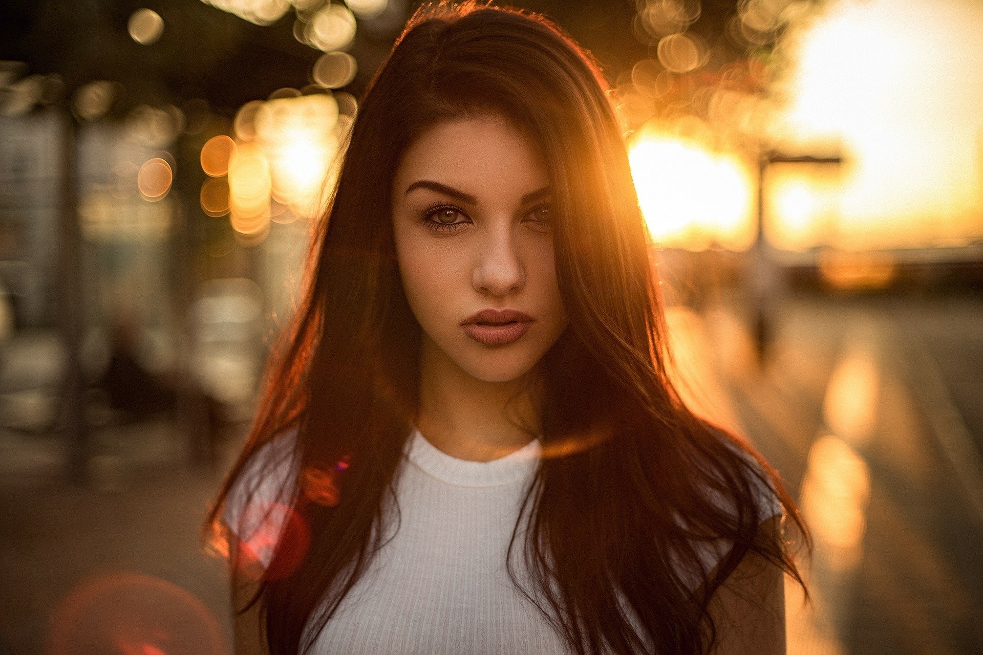 HD PC desktop wallpaper: close-up portrait of a brunette model with brown eyes, long hair, warm sunset backlight and shallow depth of field.
