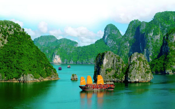 A traditional boat sails through the turquoise waters of Ha Long Bay, Vietnam, surrounded by towering limestone karsts under a clear sky.