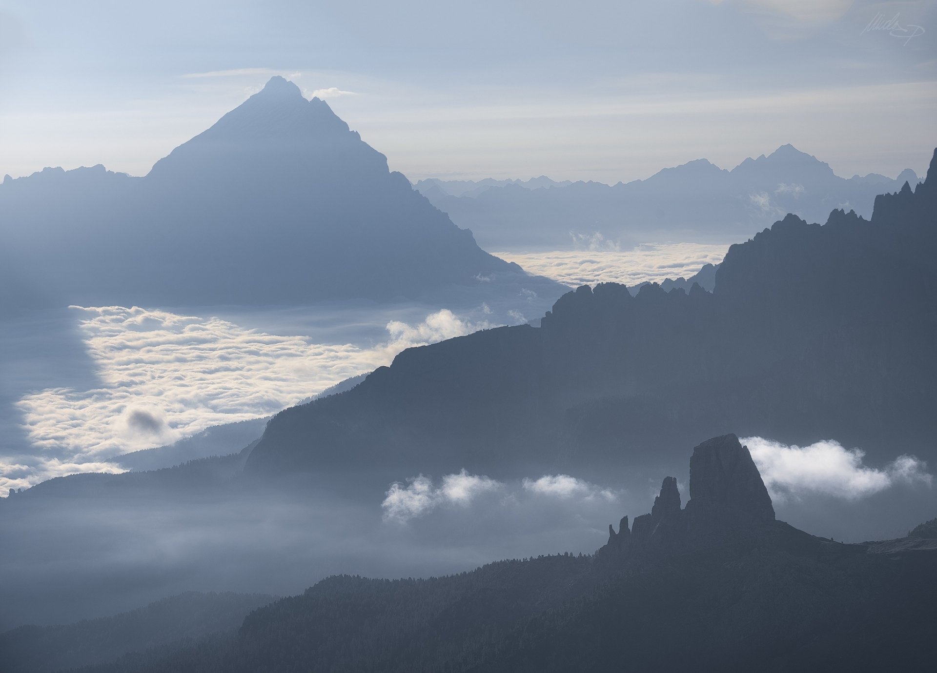 HD PC desktop wallpaper: mountain landscape — nature scene of layered blue-gray peaks rising above a sea of clouds, soft morning light and misted horizons.