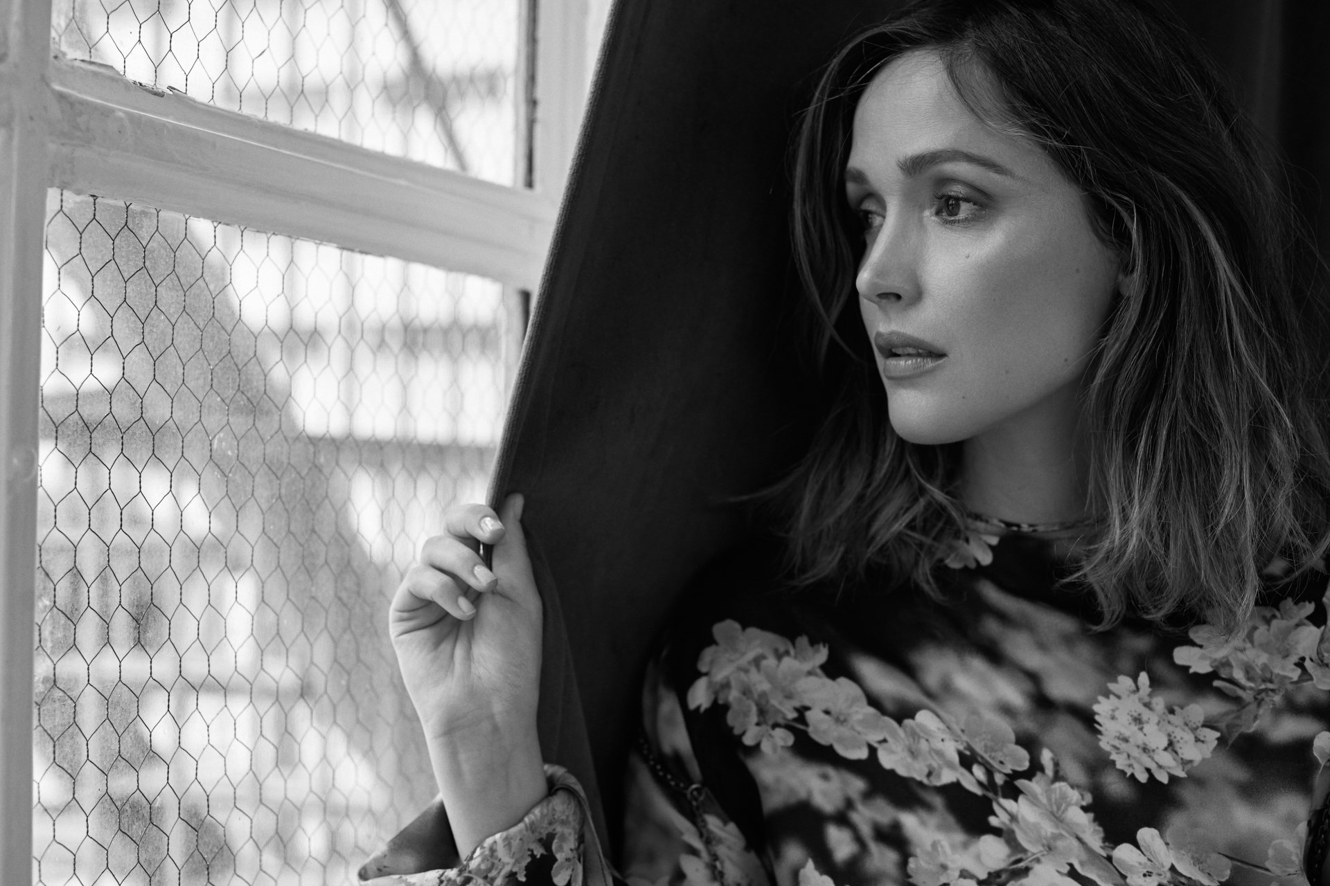 Black-and-white 2K desktop wallpaper: portrait of an unnamed Australian actress gazing from a window, floral top, hand lifting a coat.