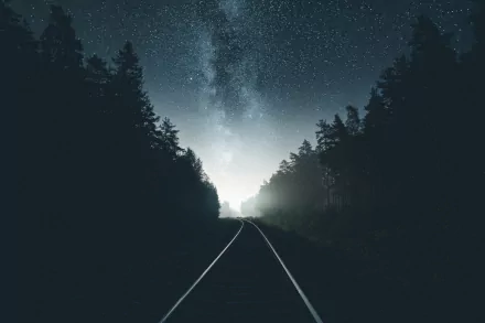 HD desktop wallpaper featuring a starry night sky over a quiet railroad, surrounded by dense trees.