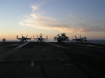 A dramatic sunset backdrop highlighting military aircraft lined up on an aircraft carrier, capturing a moment of power and tranquility at sea.