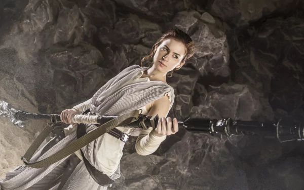 Cosplayer dressed as Rey from Star Wars holding her staff in a rocky cave — 5K Ultra HD PC desktop wallpaper.