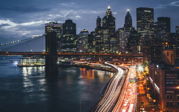 Nighttime HD desktop wallpaper showcasing the Brooklyn Bridge and Manhattan skyline with illuminated skyscrapers and light trails in New York City, USA.
