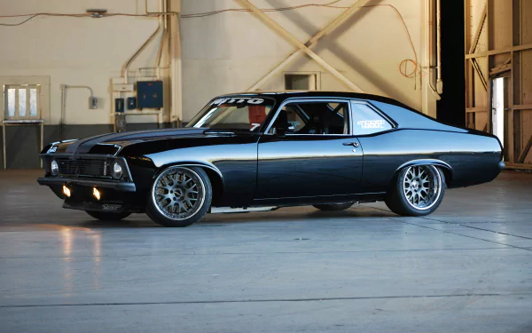 HD PC desktop wallpaper of a sleek Chevrolet Nova hot rod parked indoors, showcasing its polished black exterior and custom wheels in a spacious garage setting.