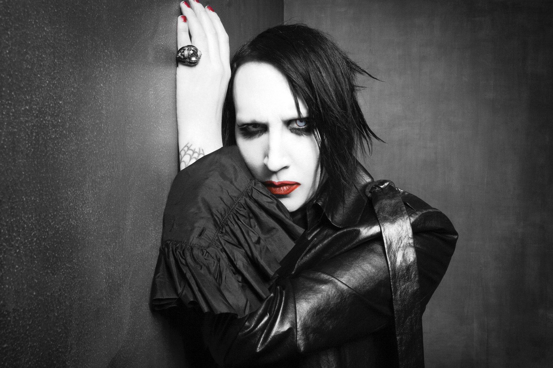 Black-and-white 2K Quad HD desktop wallpaper of a gothic industrial metal musician with pale makeup, heavy eye shadow, red lips and leather jacket in a moody studio portrait.