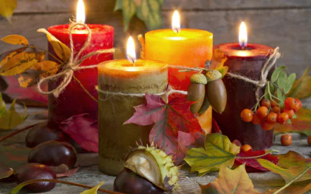 A still life of vibrant fall colors featuring lit candles surrounded by chestnuts, acorns, and colorful leaves, creating a cozy autumn atmosphere.