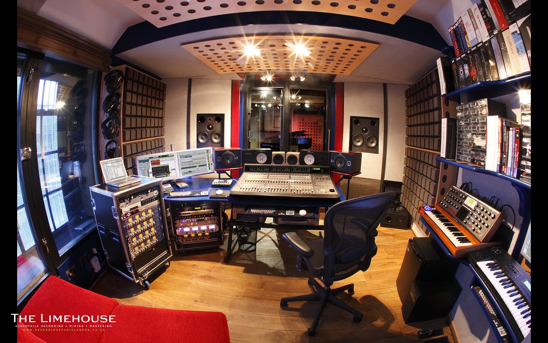 HD desktop wallpaper of a man-made recording studio room, featuring audio equipment, mixing consoles, speakers, and shelves filled with gear and books.