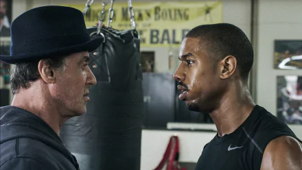 HD PC desktop wallpaper from the movie Creed: veteran trainer Rocky Balboa facing off with boxer Adonis Creed in a gritty gym, intense eye contact before a fight.