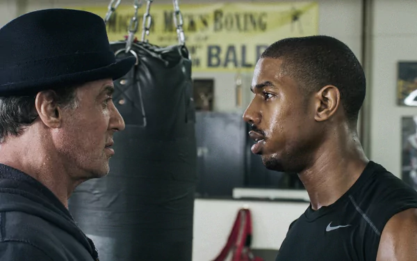 HD PC desktop wallpaper from the movie Creed: veteran trainer Rocky Balboa facing off with boxer Adonis Creed in a gritty gym, intense eye contact before a fight.