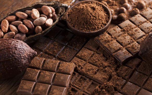 Close-up 4K Ultra HD wallpaper of rich chocolate bars, cocoa powder, and cocoa beans arranged on a dark surface, highlighting the textures and deep brown tones.