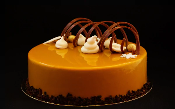 A beautifully crafted cake with a glossy caramel finish, topped with elegant chocolate curls and delicate cream swirls, set against a striking black background. A stunning 4K Ultra HD wallpaper.