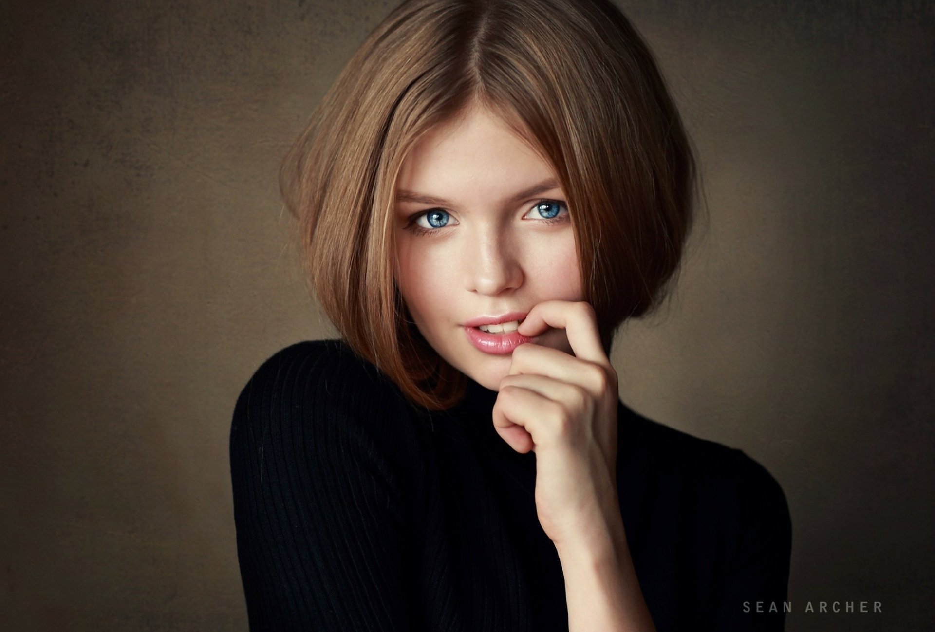 HD desktop wallpaper featuring a brunette woman with striking blue eyes, posing thoughtfully against a muted background.