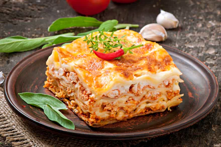A delicious slice of lasagna with layers of pasta, meat, and cheese garnished with herbs and a chili pepper, captured in stunning 4K Ultra HD for a PC wallpaper.