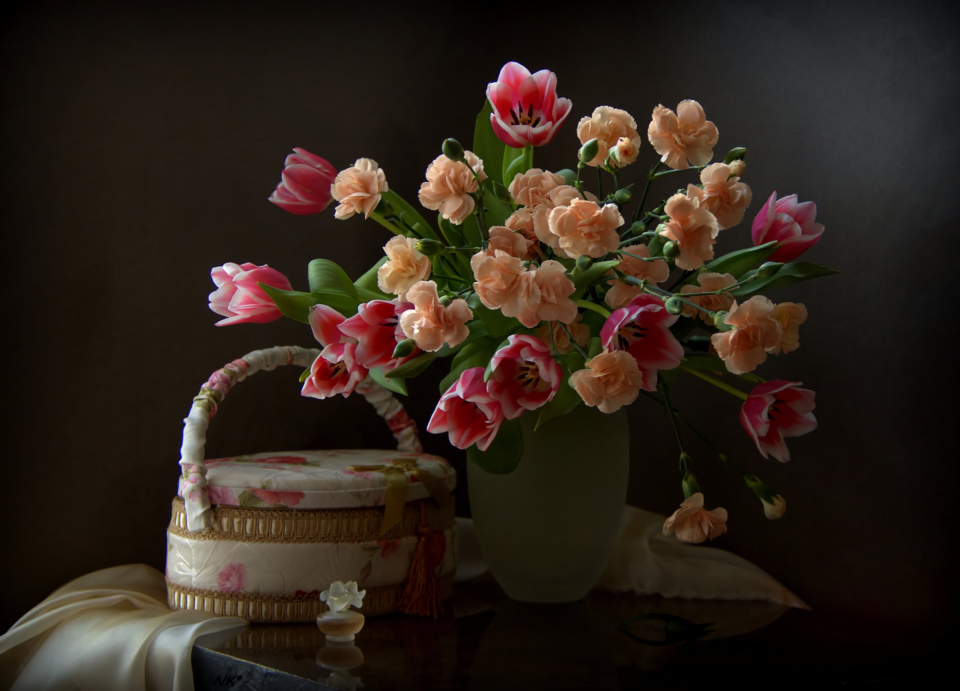 A colorful still life HD desktop wallpaper featuring a basket and a bouquet of pink tulips and peach carnations against a dark background.