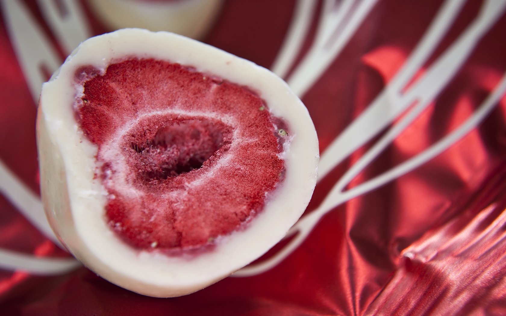 Close-up of a half-cut sweet, showcasing vibrant red fruit encased in smooth white chocolate. The image serves as a delicious backdrop for food and sweets enthusiasts.