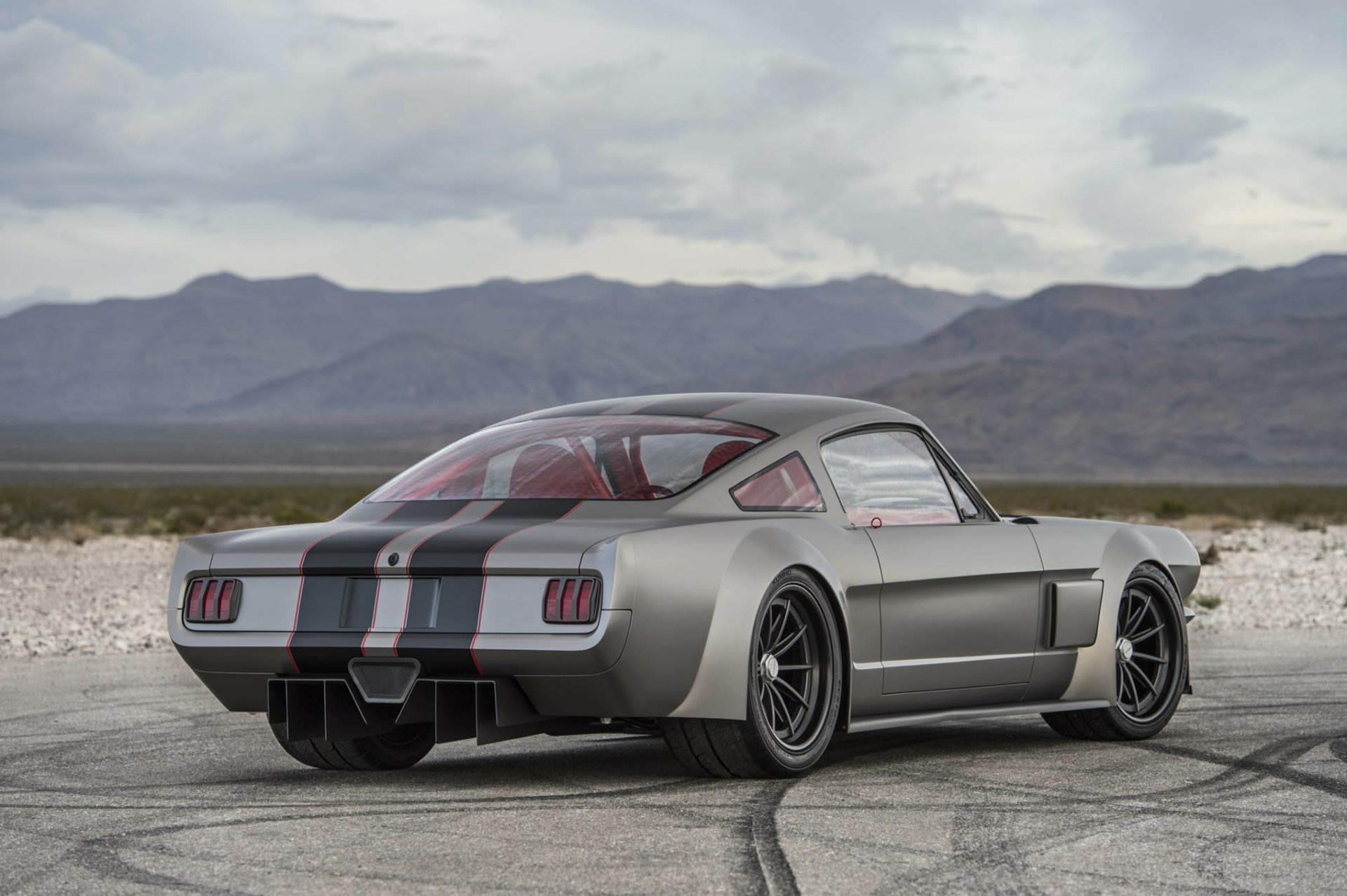HD desktop wallpaper featuring a sleek Ford Mustang Fastback muscle car hot rod parked on a cracked desert road with mountains in the background.