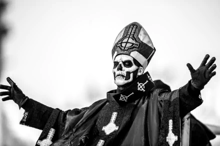 HD desktop wallpaper featuring Ghost B.C., a heavy metal band, with a member dressed in an intricate costume and skull makeup, arms outstretched. The monochrome image captures the dramatic essence of their performance.
