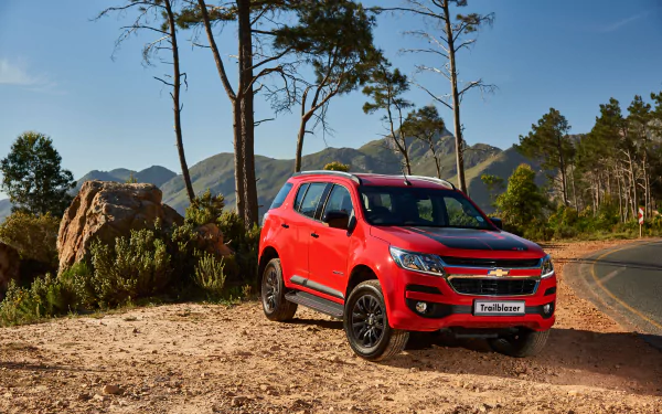 A red Chevrolet TrailBlazer SUV parked on a dirt path by a winding road with trees and mountains in the background, captured in 4K Ultra HD quality.