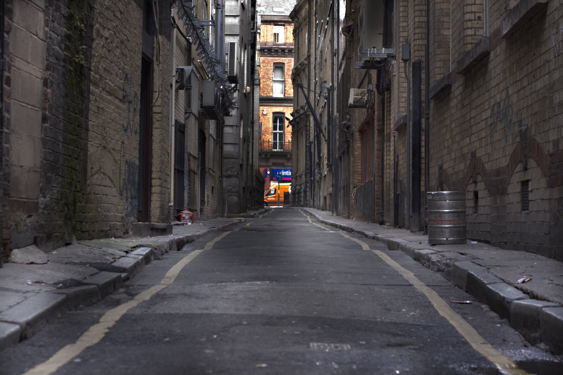 4K Ultra HD image of a narrow man-made alley between brick buildings, with a view of a lit storefront in the distance under overcast lighting.