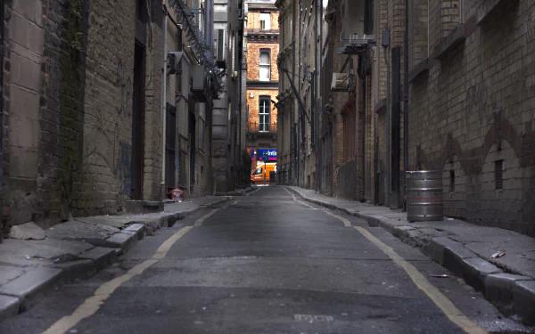 4K Ultra HD image of a narrow man-made alley between brick buildings, with a view of a lit storefront in the distance under overcast lighting.