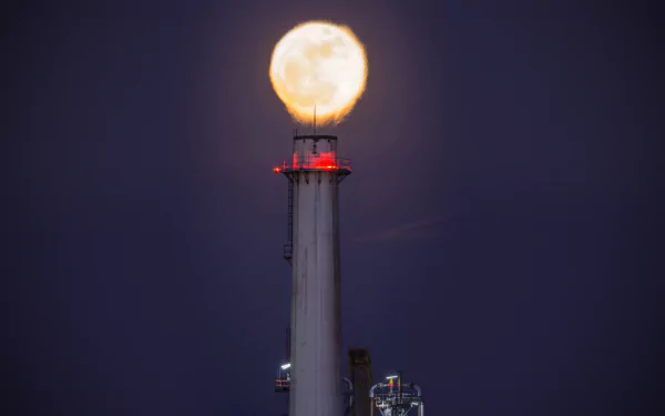 HD PC desktop wallpaper: a factory chimney at night with the full moon perched like a glowing cap, industrial lights below against a natural deep night sky.