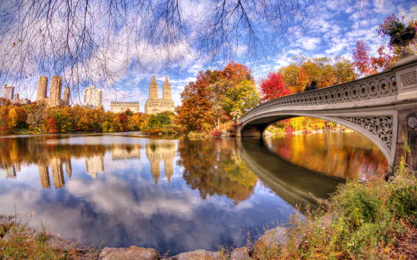 HD desktop wallpaper of Bow Bridge in New York during fall, showing vibrant autumn trees reflected in the calm pond beneath the man-made arched bridge.