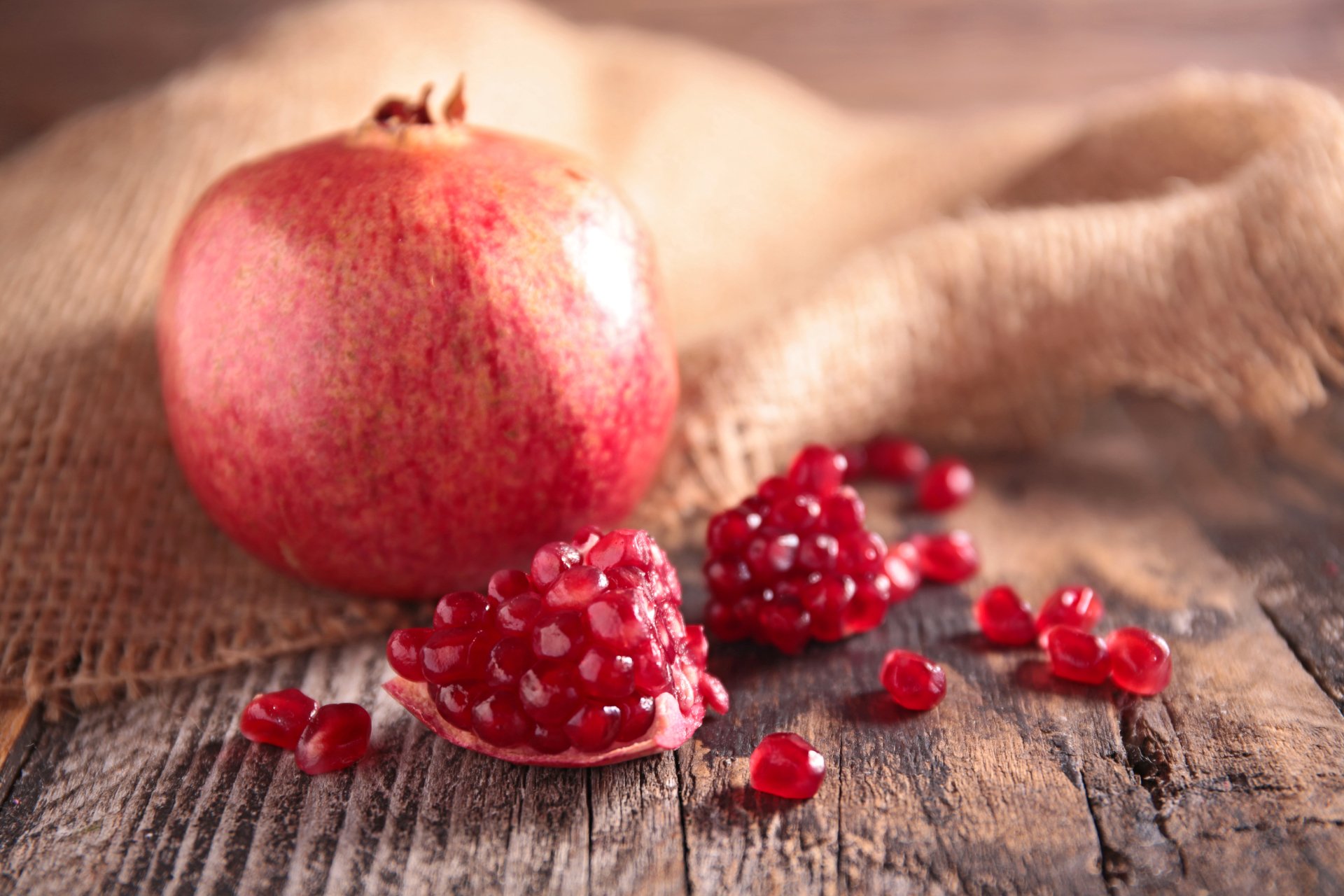 A vibrant pomegranate with scattered seeds rests on a rustic wooden surface, captured in stunning 4K Ultra HD for a vivid PC desktop wallpaper background.