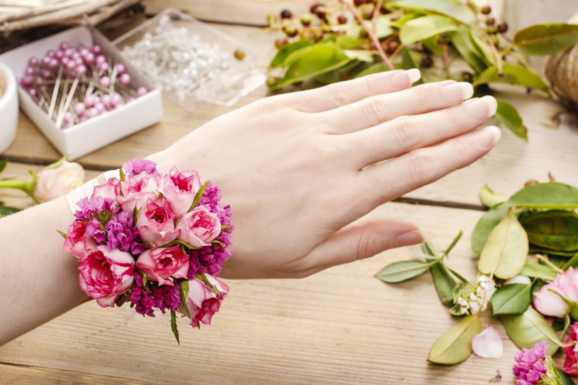 Close-up of a hand wearing a man-made pink flower wrist corsage on a wooden table, 5K Ultra HD PC desktop wallpaper background.