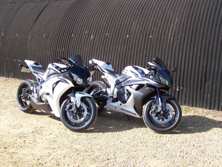 HD desktop wallpaper of two Honda motorcycles, a CBR600RR and a CBR1000RR, parked side by side against a corrugated metal background.