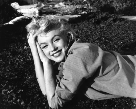 Black and white HD wallpaper of Marilyn Monroe smiling while lying on grass, exuding classic charm and elegance.