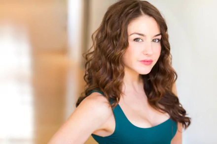 HD desktop wallpaper featuring a poised individual with curly hair and a teal top, providing an elegant background.