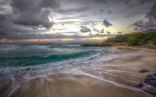 4K Ultra HD desktop wallpaper of a Hawaii beach at sunset, featuring a cloudy sky, ocean waves washing ashore, and lush greenery along the horizon.