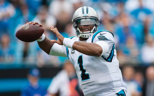 Cam Newton in action, wearing a Panthers jersey, throwing a football amidst a vibrant crowd. A dynamic sports wallpaper that captures the energy of the game.