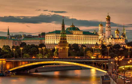 Evening view of Moscow's Kremlin and a lit bridge over the river, showcasing iconic Russian architecture in a vibrant cityscape.
