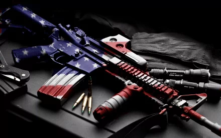 A patriotic-themed Colt AR-15 rifle, with an American flag design, surrounded by bullets and tactical gear, captured in a high-definition desktop wallpaper.