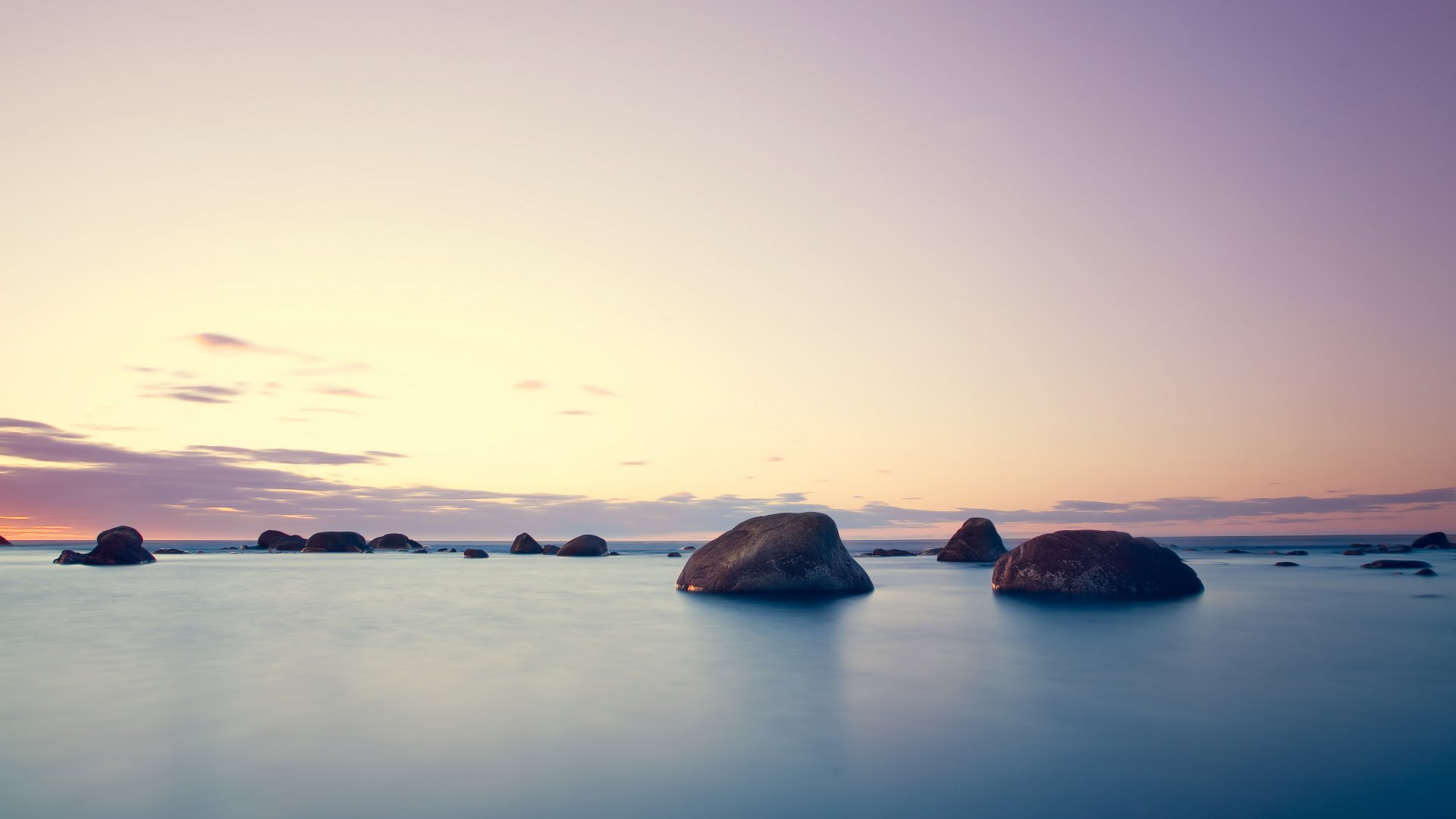A serene island landscape at dusk, featuring calm waters reflecting the sky and clouds, with smooth rocks emerging from the water. A tranquil 4K Ultra HD wallpaper for nature lovers.