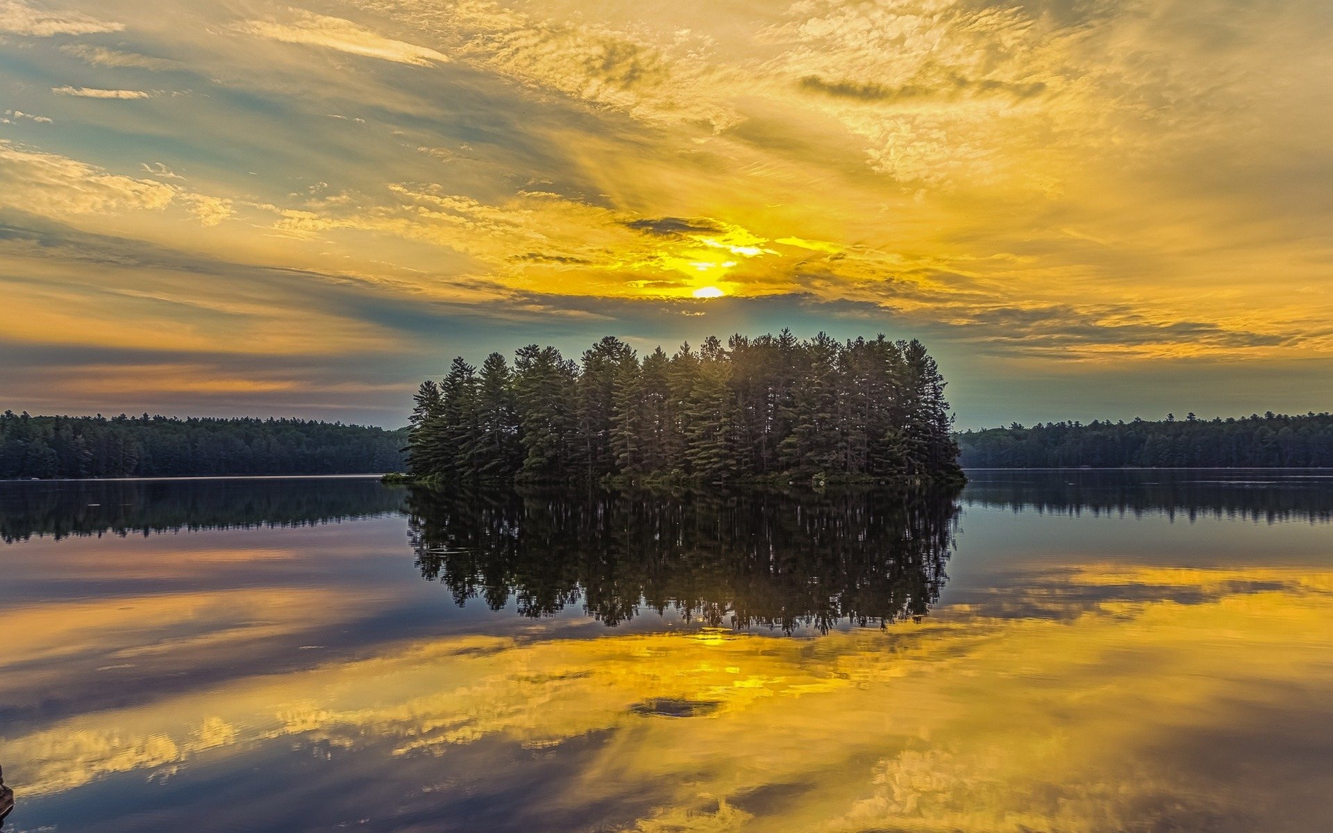A serene HD desktop wallpaper featuring a small tree-covered island reflecting on a tranquil lake under a golden, cloud-filled sky at sunset.