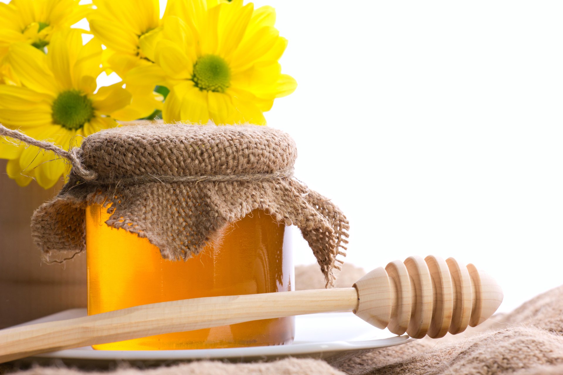 Jar of honey with a wooden honey dipper and bright yellow flowers, captured in stunning 4K Ultra HD as a vibrant PC desktop wallpaper background.