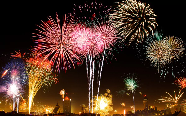 HD desktop wallpaper featuring vibrant fireworks over Leipzig, Germany. The night sky bursts into a colorful display, illuminating the city's silhouette below. A stunning piece of photography capturing festive fireworks.