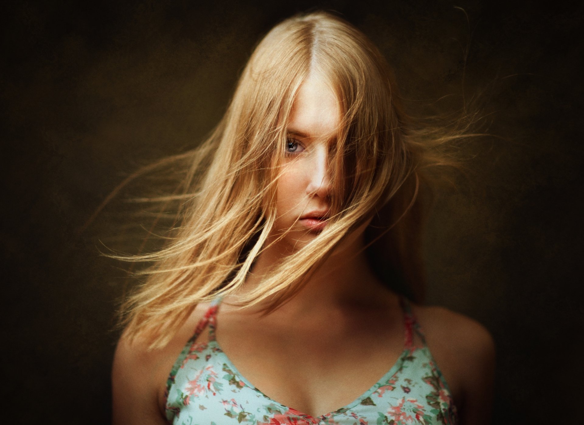 HD desktop wallpaper featuring a blonde woman model with long hair and striking blue eyes against a dark, blurred background.