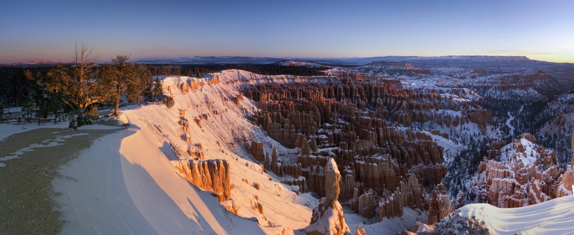 Winter landscape of Bryce Canyon National Park in Utah, showcasing snow-covered cliffs and deep canyon formations under a clear sky, captured in high definition.