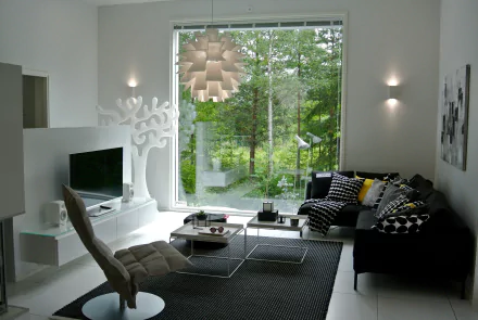 Modern living room with stylish furniture, featuring a TV, cushioned chair, and decorative cushions. Large window offers a serene view of greenery, enhancing the room's relaxing ambiance. HD wallpaper.