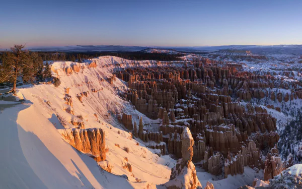Winter landscape of Bryce Canyon National Park in Utah, showcasing snow-covered cliffs and deep canyon formations under a clear sky, captured in high definition.