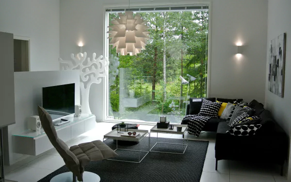 Modern living room with stylish furniture, featuring a TV, cushioned chair, and decorative cushions. Large window offers a serene view of greenery, enhancing the room's relaxing ambiance. HD wallpaper.
