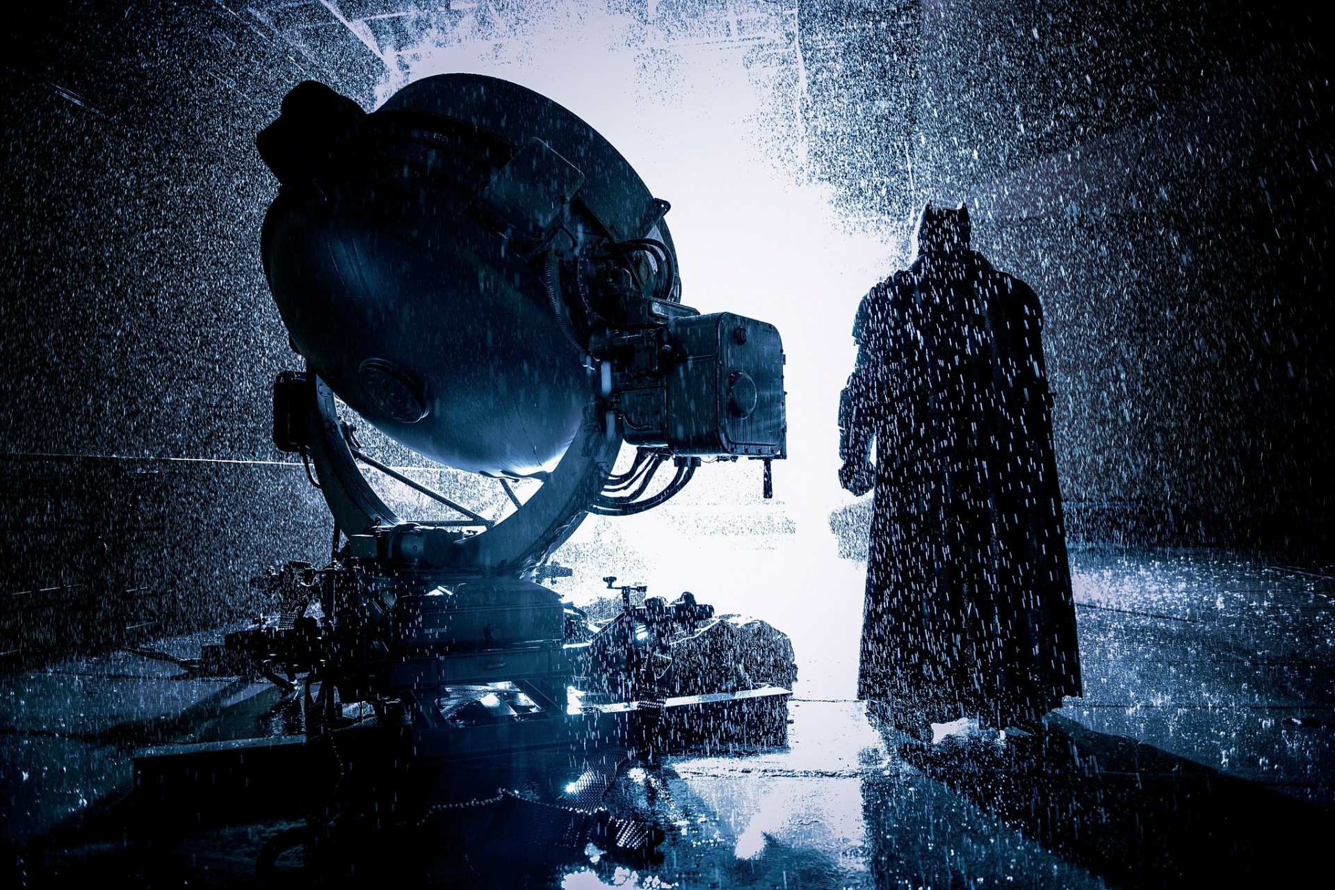 A dark, rainy scene from Batman v Superman: Dawn of Justice featuring Batman standing near the illuminated Bat-Signal, captured in HD for a PC desktop wallpaper.