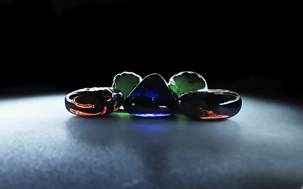 An artistic HD wallpaper featuring a collection of light-reflecting glass pebbles in blue, emerald, and amber hues arranged on a dark background.