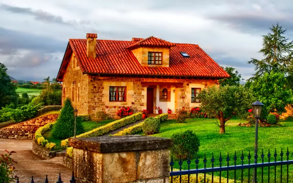 HD desktop wallpaper featuring a charming countryside house in England, surrounded by a manicured garden with vibrant flowers, a tree, and a fence. The peaceful field in the background completes the scene.